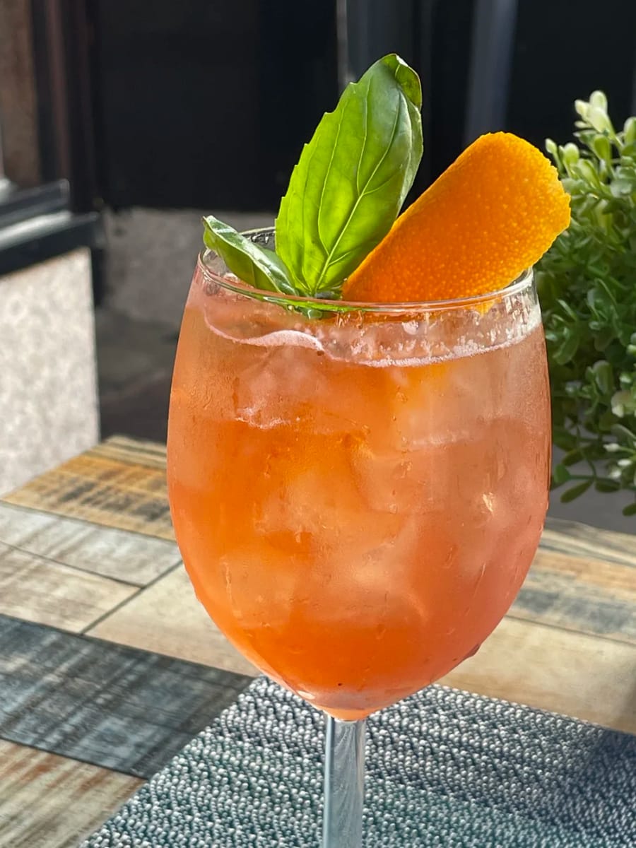 A cocktail garnished with basil and an orange peel