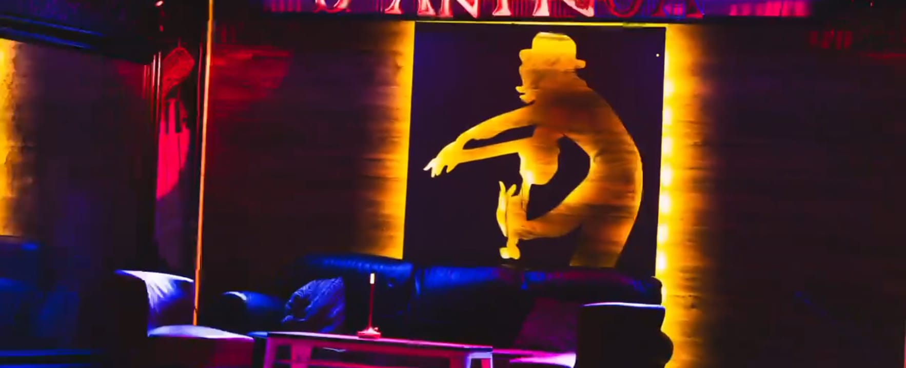 The gold neon silhouette sign glowing behind the lounge sofas at D'Antigua
